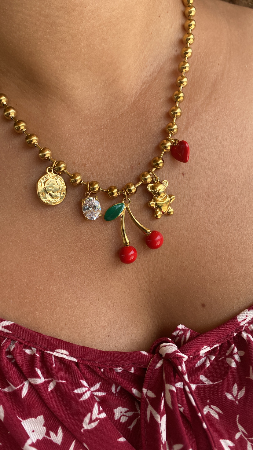 Colar dourado com pendentes variados usado junto do pescoço.