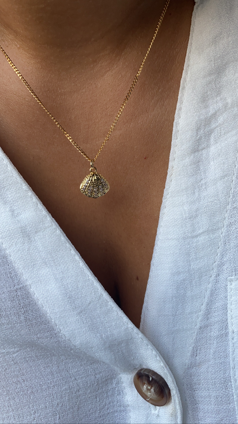 Colar dourado com pendente de concha numa camisa branca