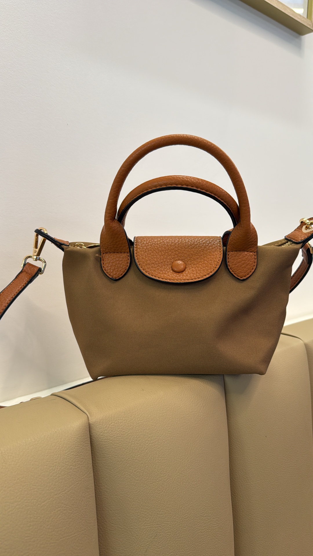 Mala pequena de mão castanha em tecido e pele sobre cadeira bege