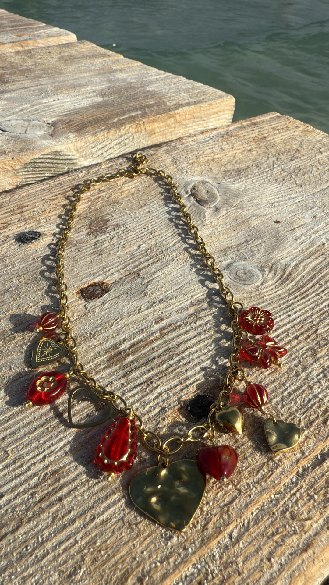 Colar dourado com pendentes vermelhos e dourados em madeira perto de água