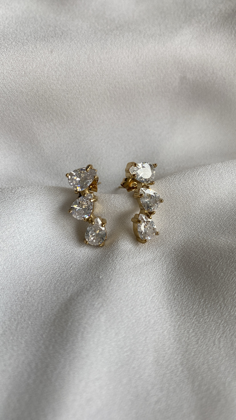 Brincos dourados com pedras transparentes sobre tecido branco