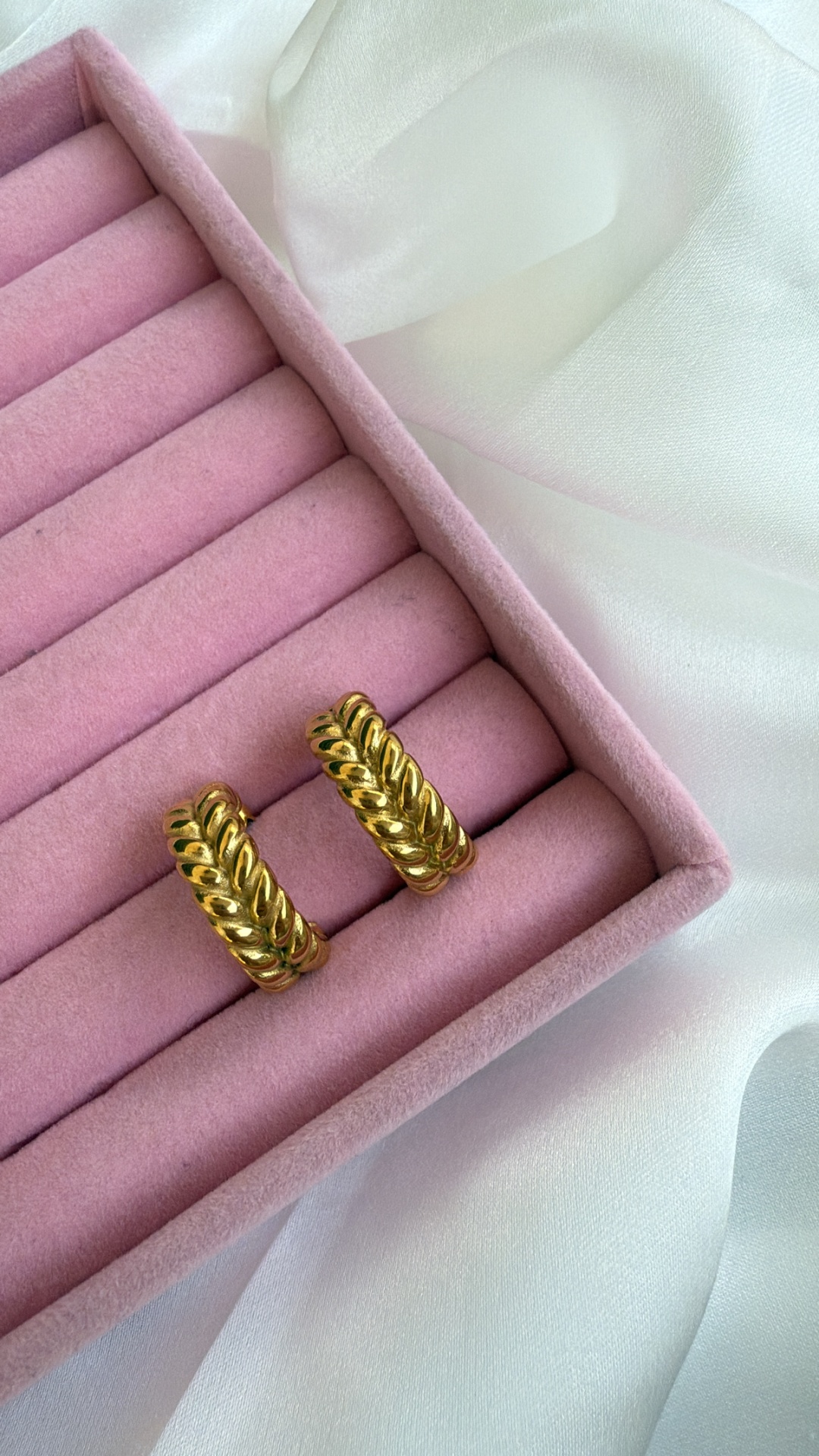 Brincos dourados ondulados numa caixa rosa sobre tecido branco