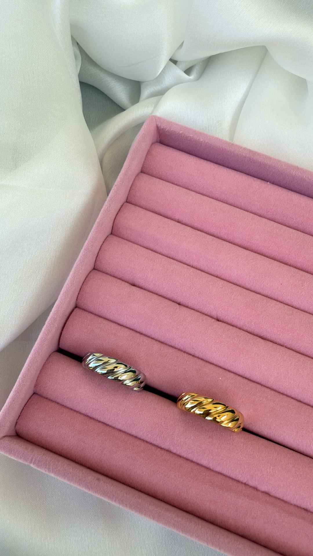 Uma caixa de veludo cor de rosa com duas argolas trançadas, uma prateada e outra dourada.