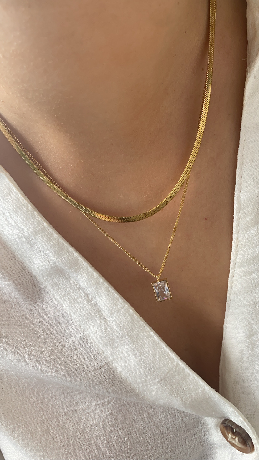 Colares dourados finos com pendente retangular translúcido sobre camisa branca