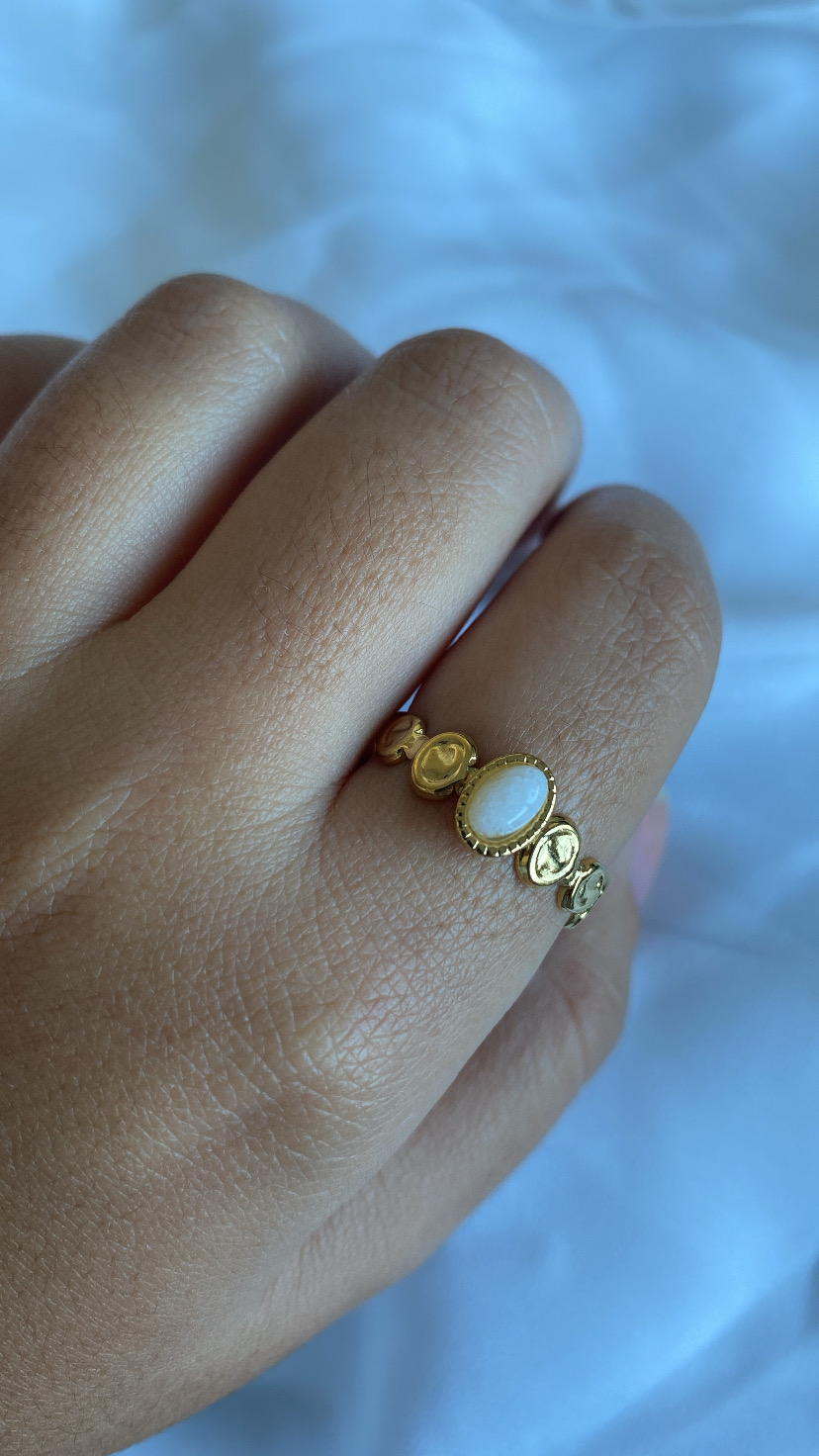 Anel dourado com pedra branca num dedo