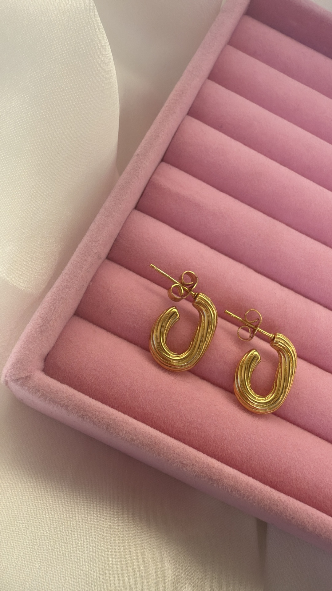 Par de brincos dourados numa caixa de veludo rosa