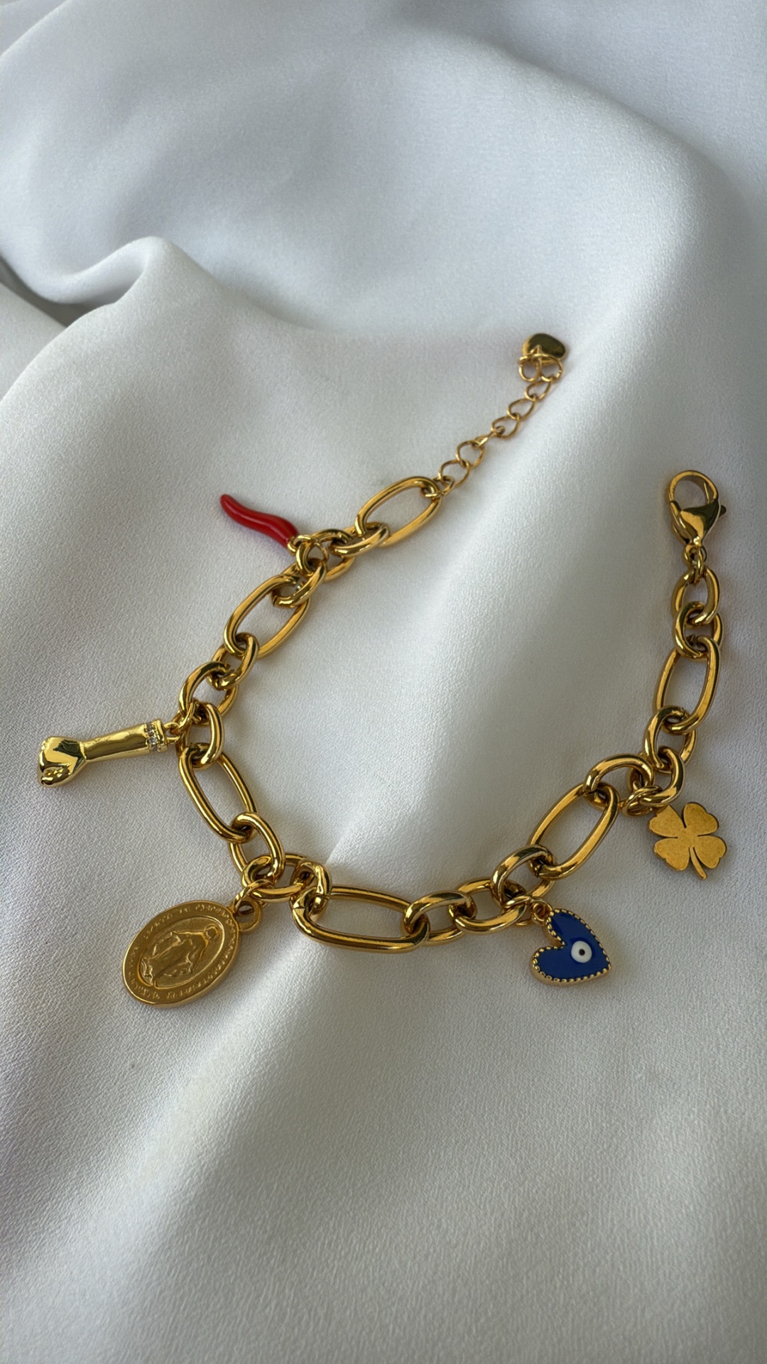 Pulseira dourada com vários pendentes sobre tecido branco
