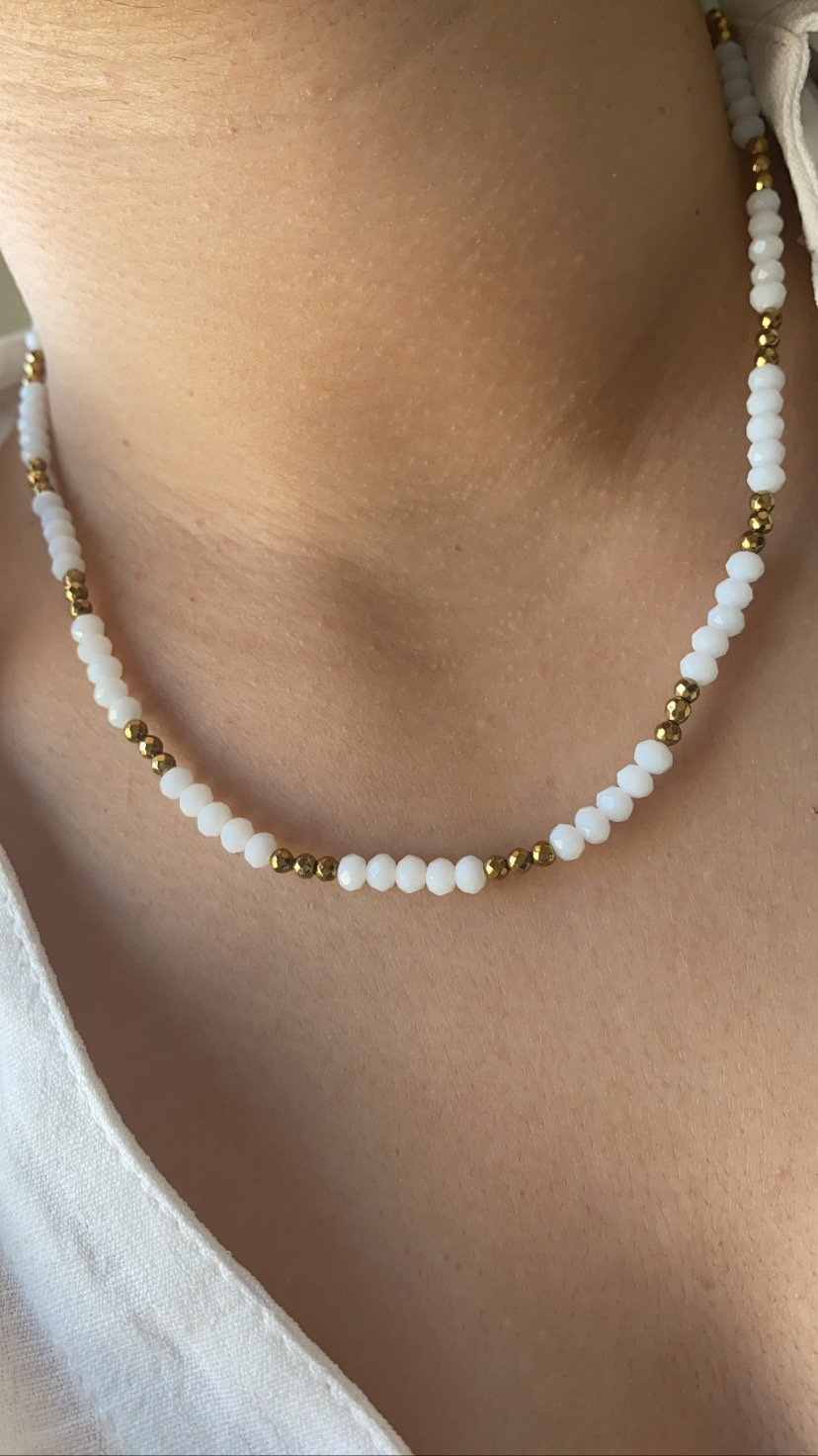 Colar com contas brancas e douradas no pescoço