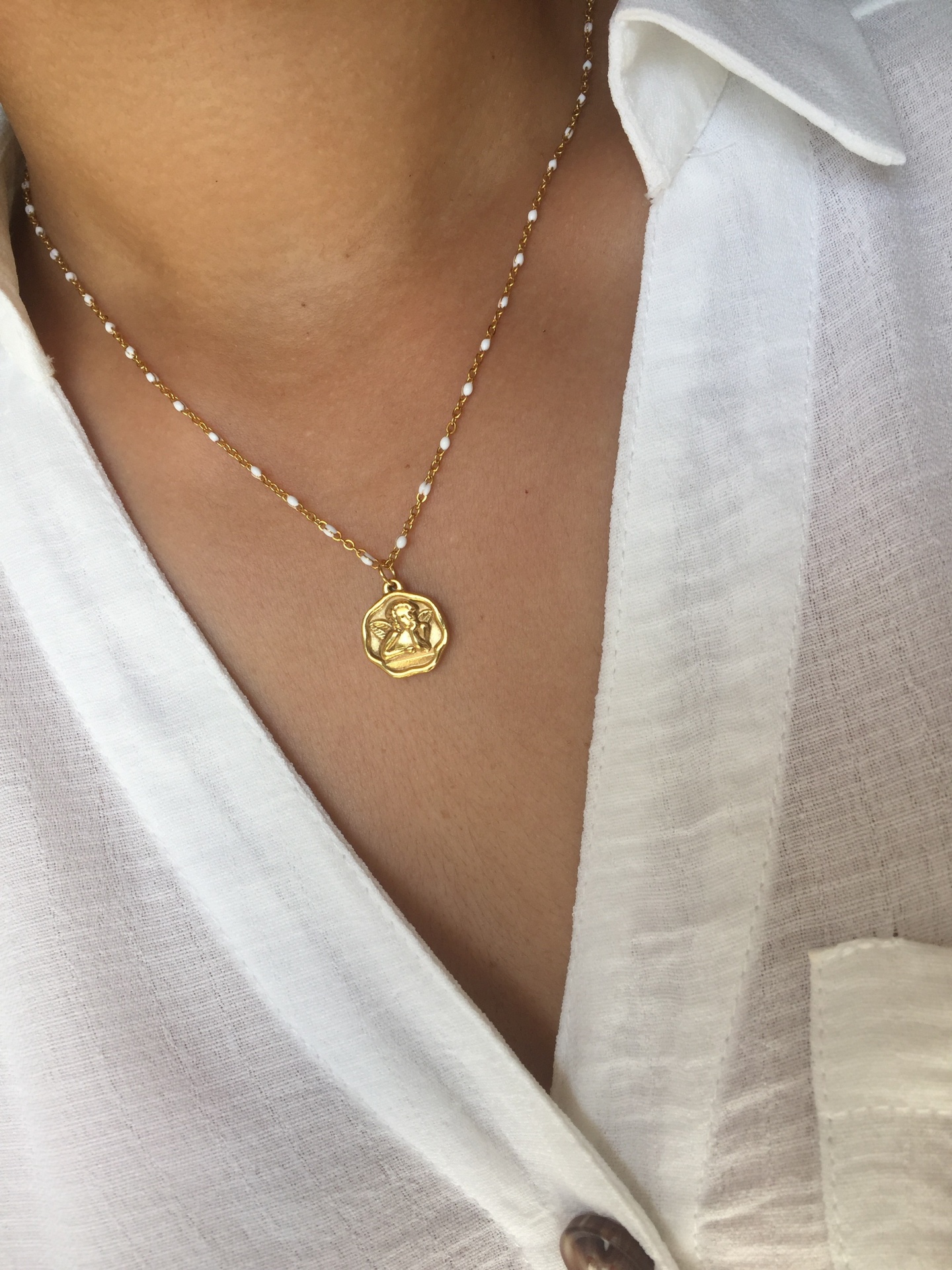 Colar dourado com pendente e pérolas em cima de camisa branca de linho