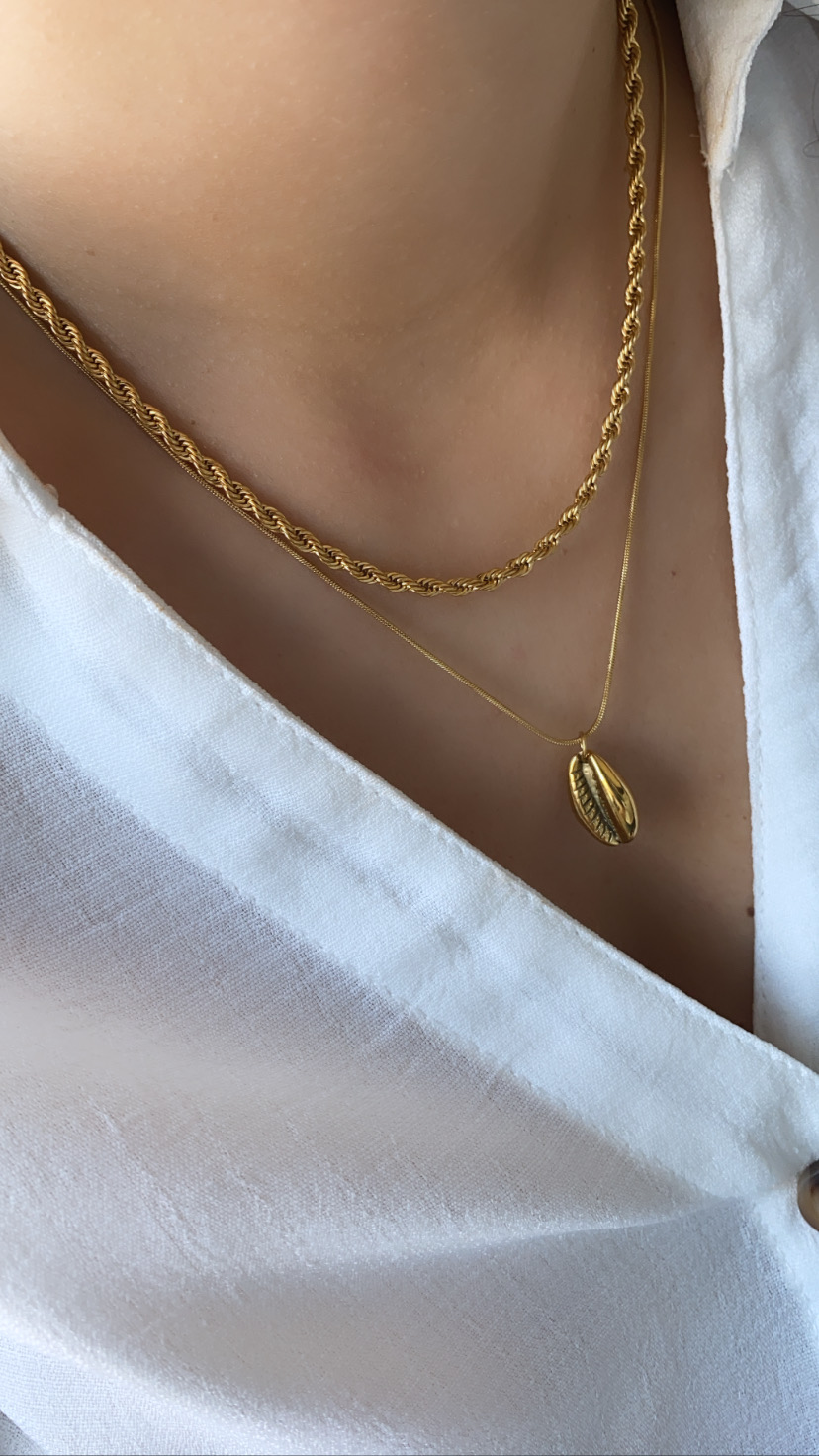 Duas colares dourados em pescoço com camisa branca