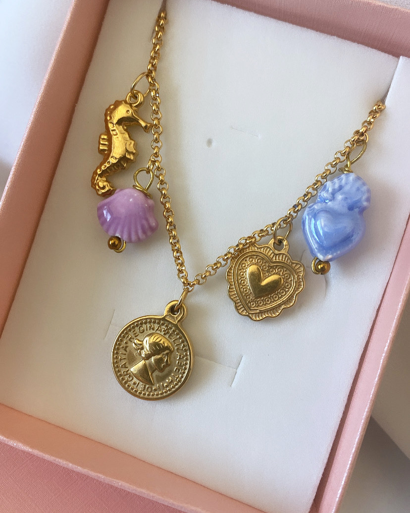 Colar dourado com pendentes de cavalo-marinho, concha, moeda e medalhão em caixa rosa
