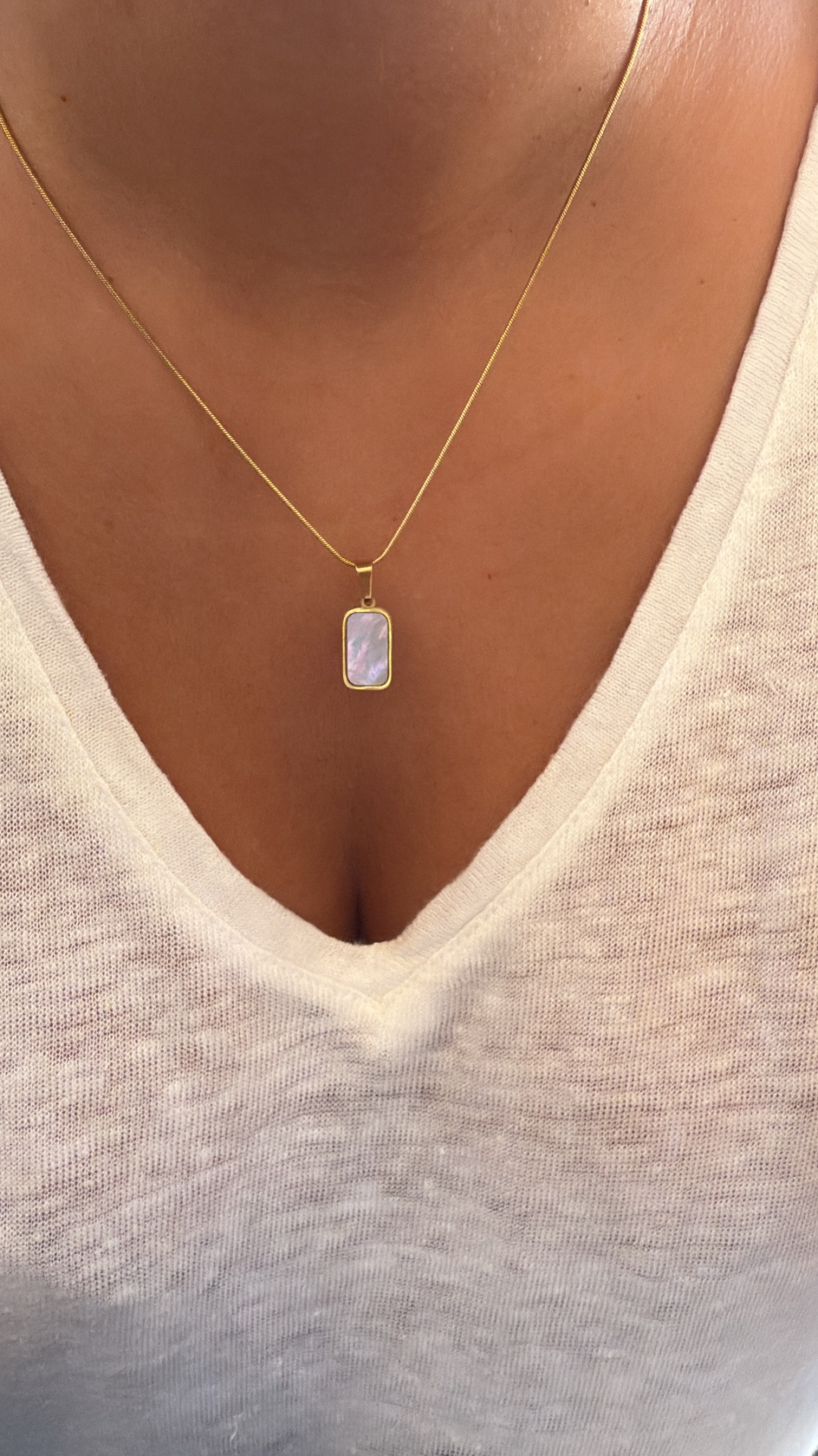 Colar dourado com pendente retangular de madrepérola e camisola branca
