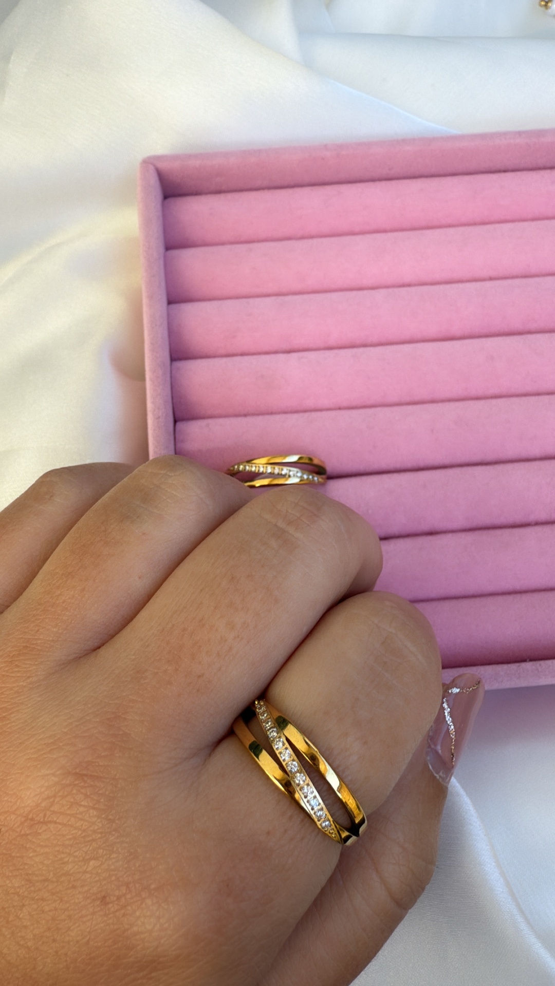 Anel dourado com pedras em dedo feminino e caixa rosa acolchoada