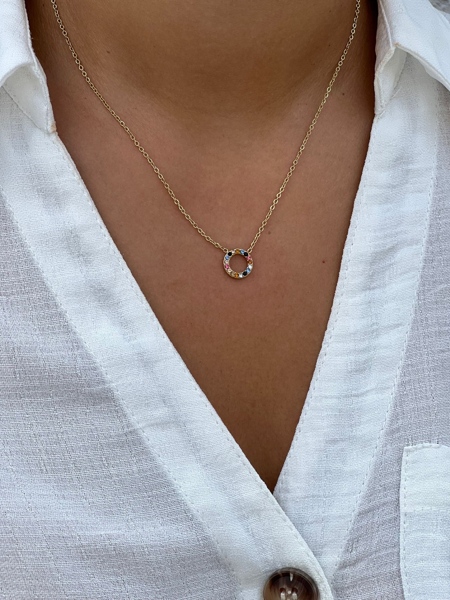 Colar dourado com pendente circular colorido usado com camisa branca