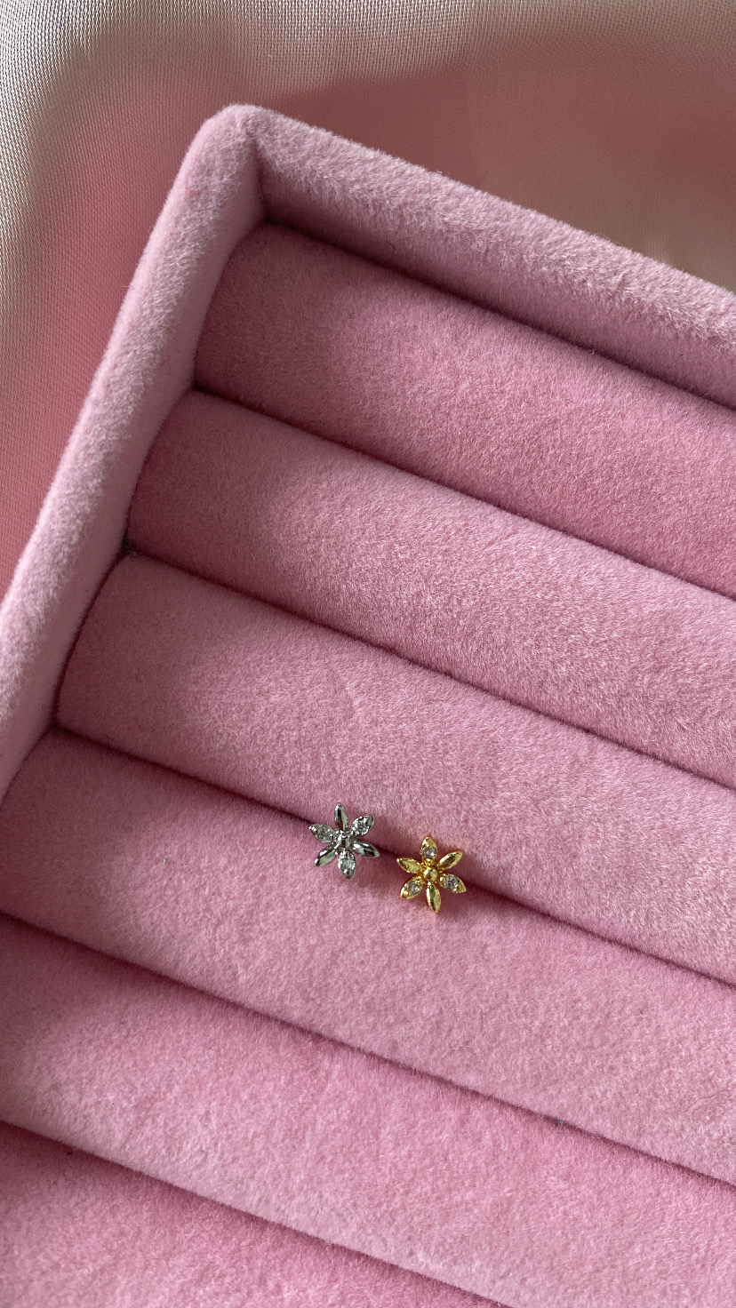 Brincos pequenos em forma de flor prateado e dourado numa caixa de veludo rosa
