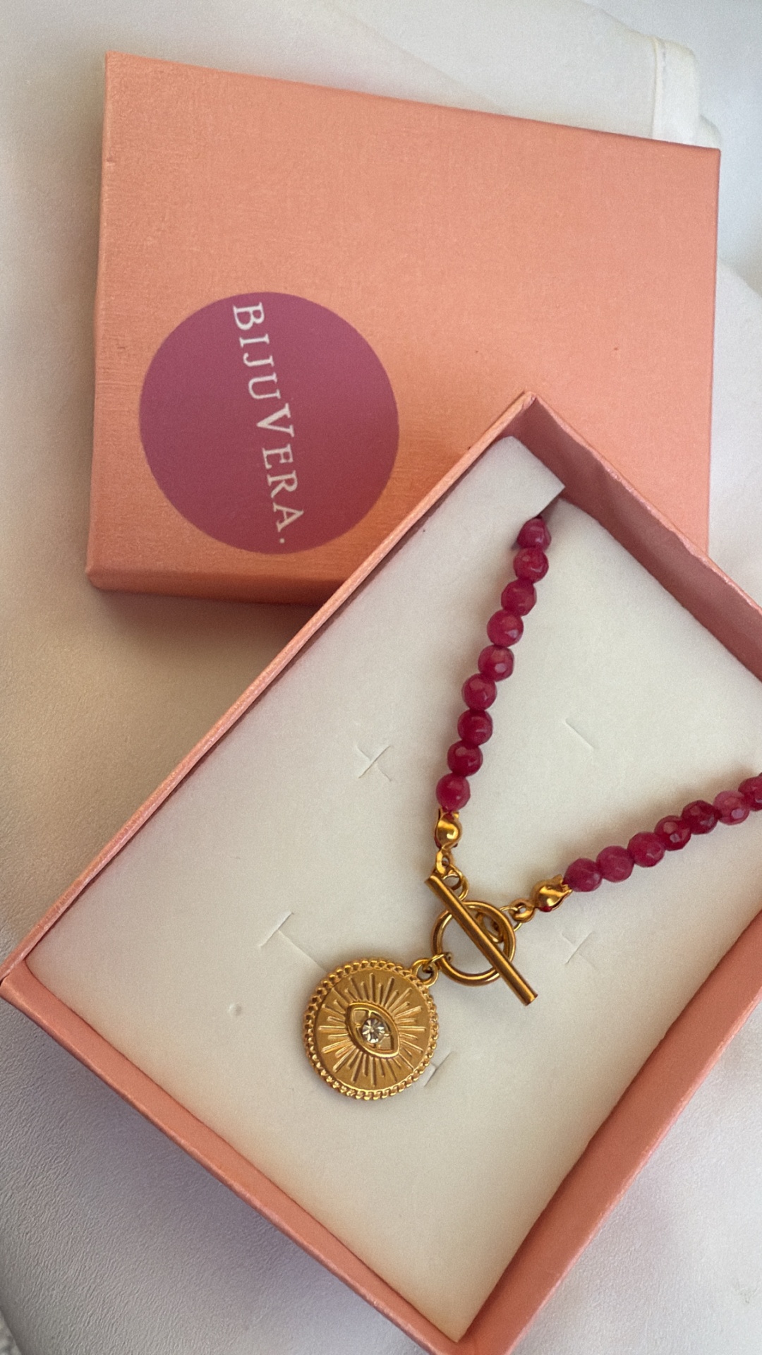 Colar com contas vermelhas e pendente dourado numa caixa rosa BIJUVERA