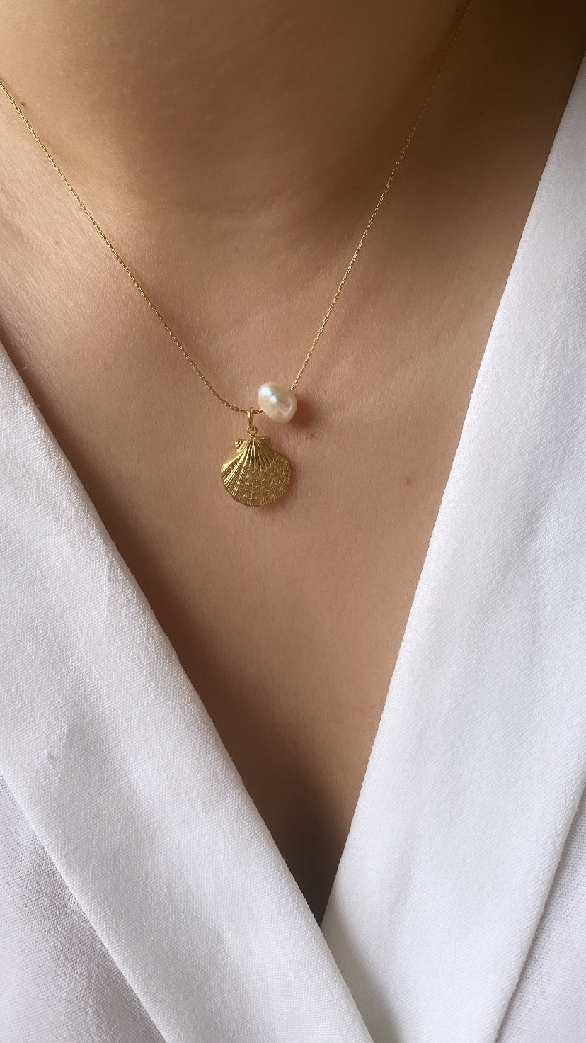 Colar com concha dourada e pérola em pescoço com vestido branco