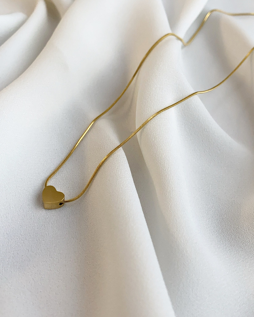 Colar dourado com pendente em forma de coração sobre tecido branco