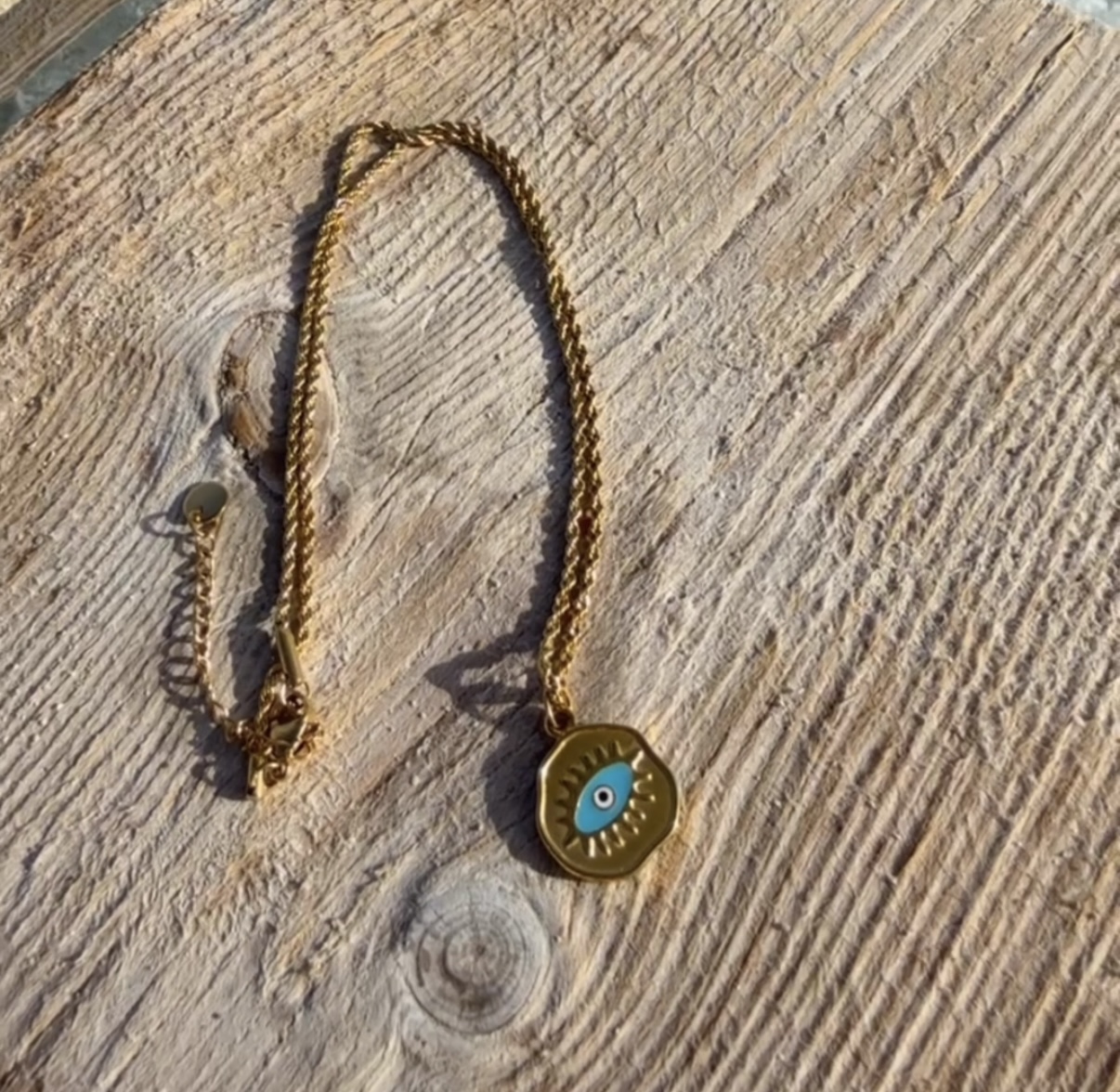 Colar dourado com pendente de olho azul sobre madeira clara