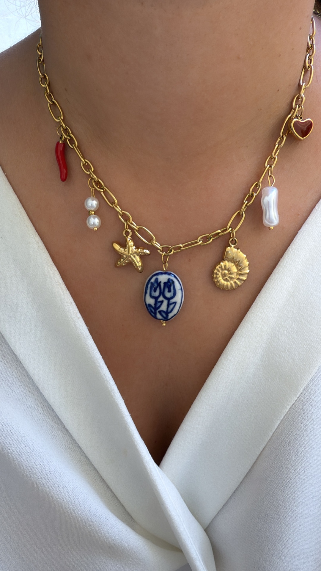 Colar dourado com pendentes coloridos e pérolas sobre camisa branca