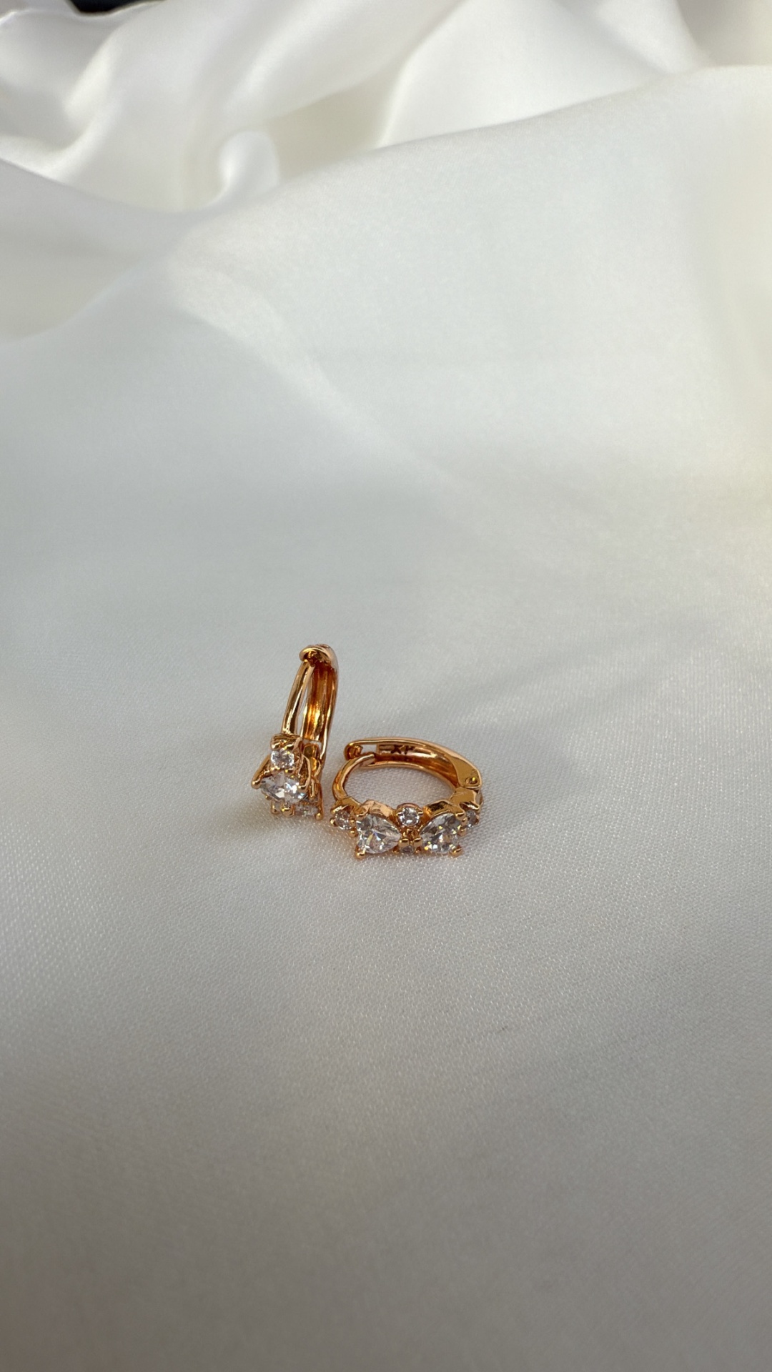 Brincos dourados com pedras transparentes sobre tecido branco