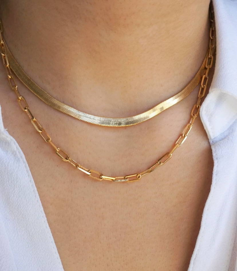 Duas correntes douradas de metal no pescoço de uma pessoa com camisa branca