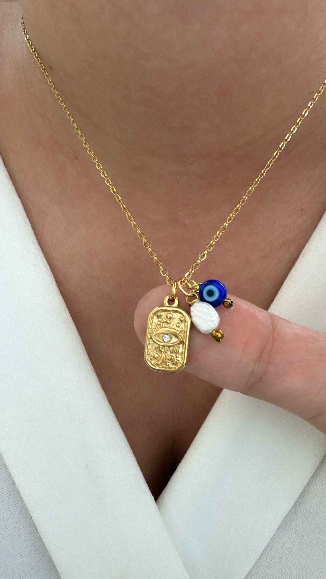 Colar dourado com pendente de olho, conta azul e duas pequenas contas, usado sobre roupa branca