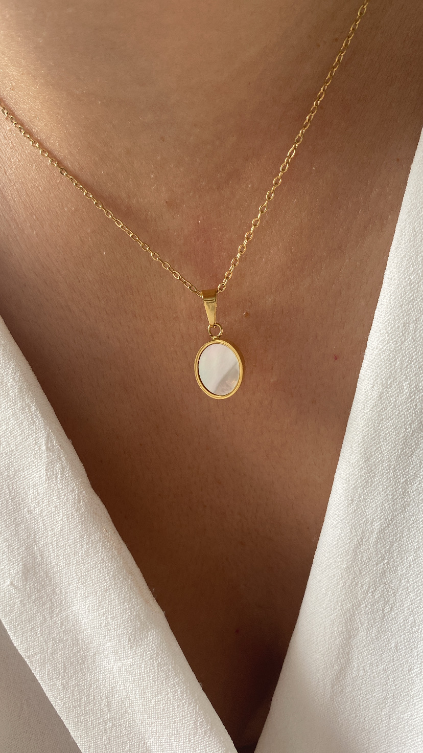 Colar dourado com pendente oval de madrepérola sobre pele e roupa branca