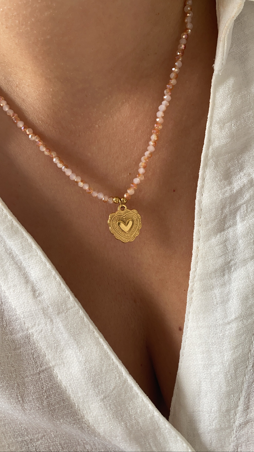 Colar de contas rosa com pendente dourado de coração em pessoa com blusa branca
