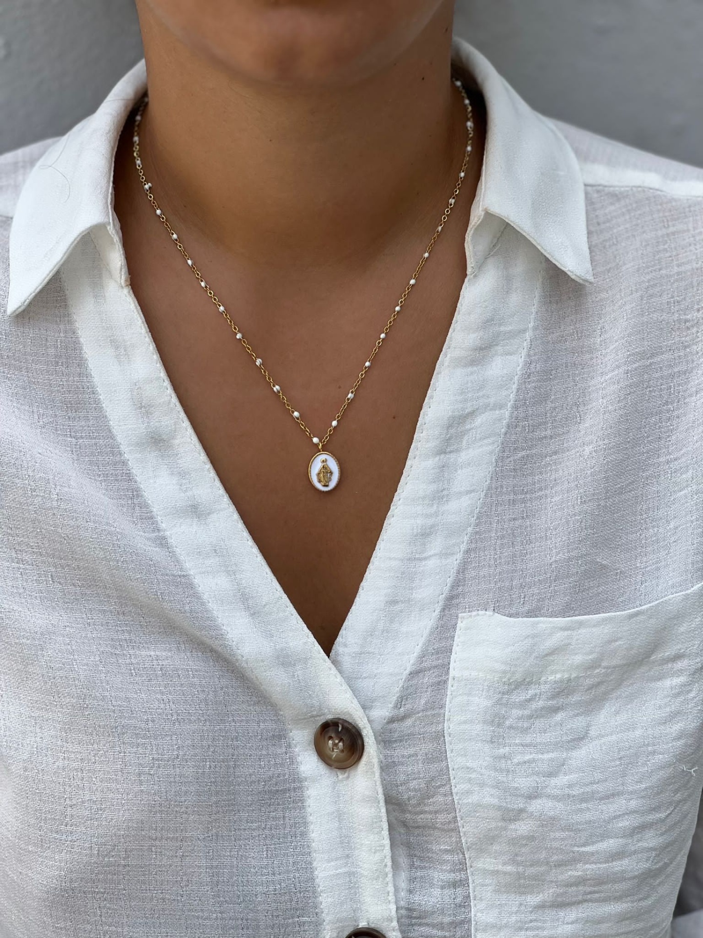 Colar dourado com pendente branco sobre camisa branca