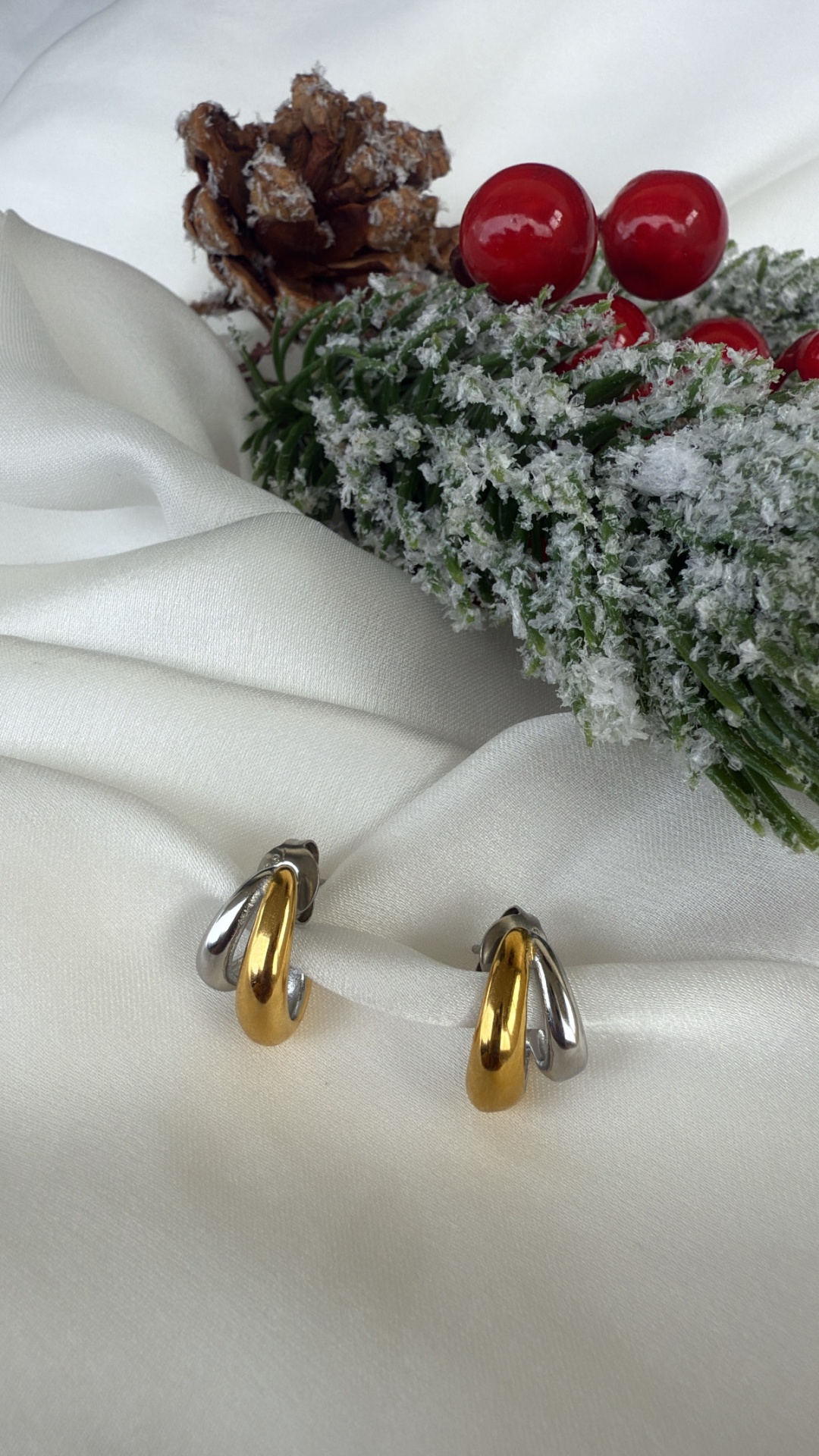 Brincos dourados e prateados sobre tecido branco com decoração de Natal ao fundo