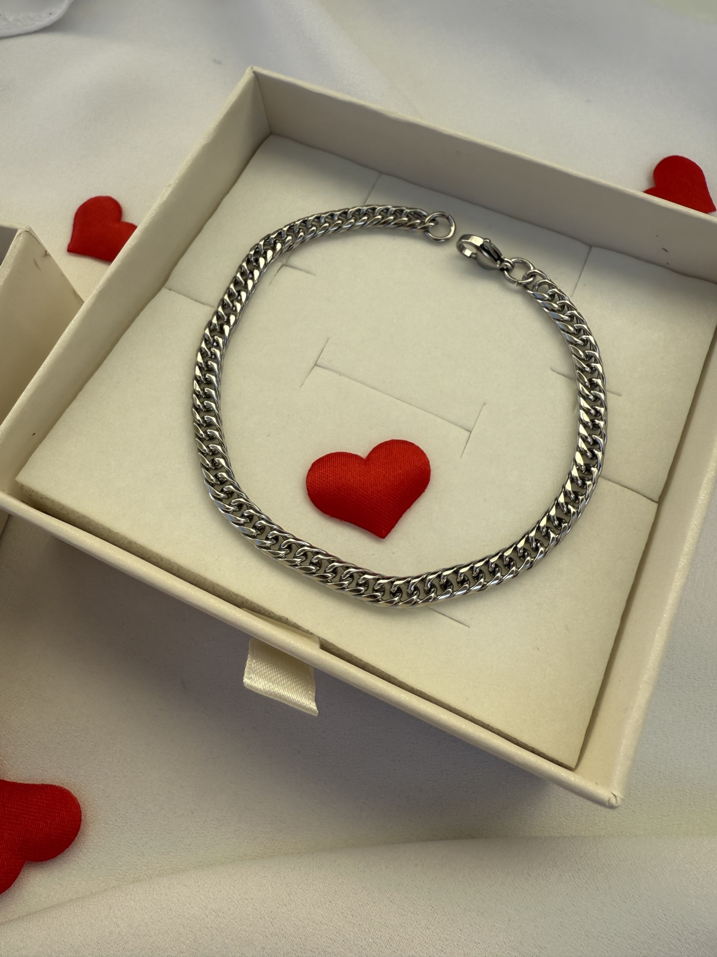 Pulseira metálica prateada com elos grossos numa caixa branca decorada com pequenos corações vermelhos
