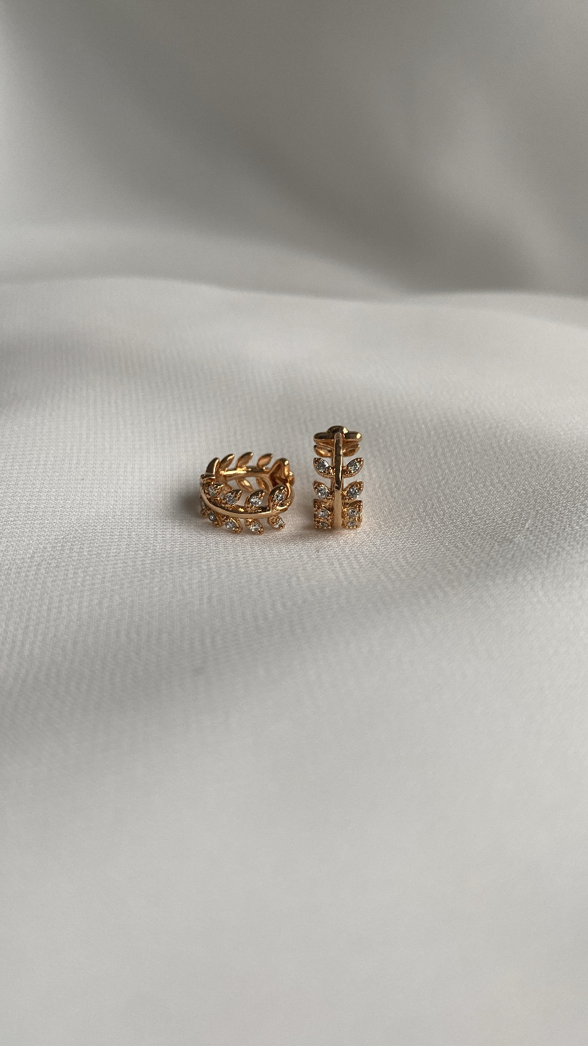 Par de brincos dourados em formato de folhas sobre tecido branco