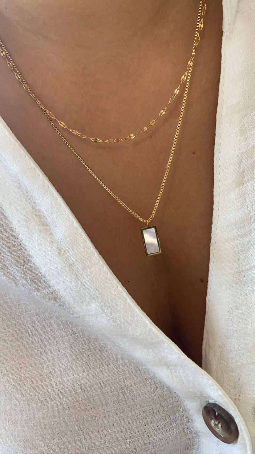 Duas correntes douradas com pendente retangular em madrepérola sobre pele e camisa branca