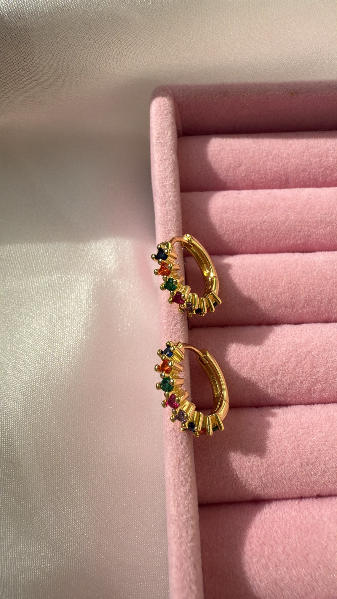 Brincos de argola dourados com pedras coloridas numa caixa de veludo rosa