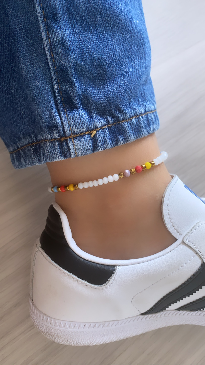 tornozeleira de contas coloridas em tornozelo com ténis branco e calça de ganga azul