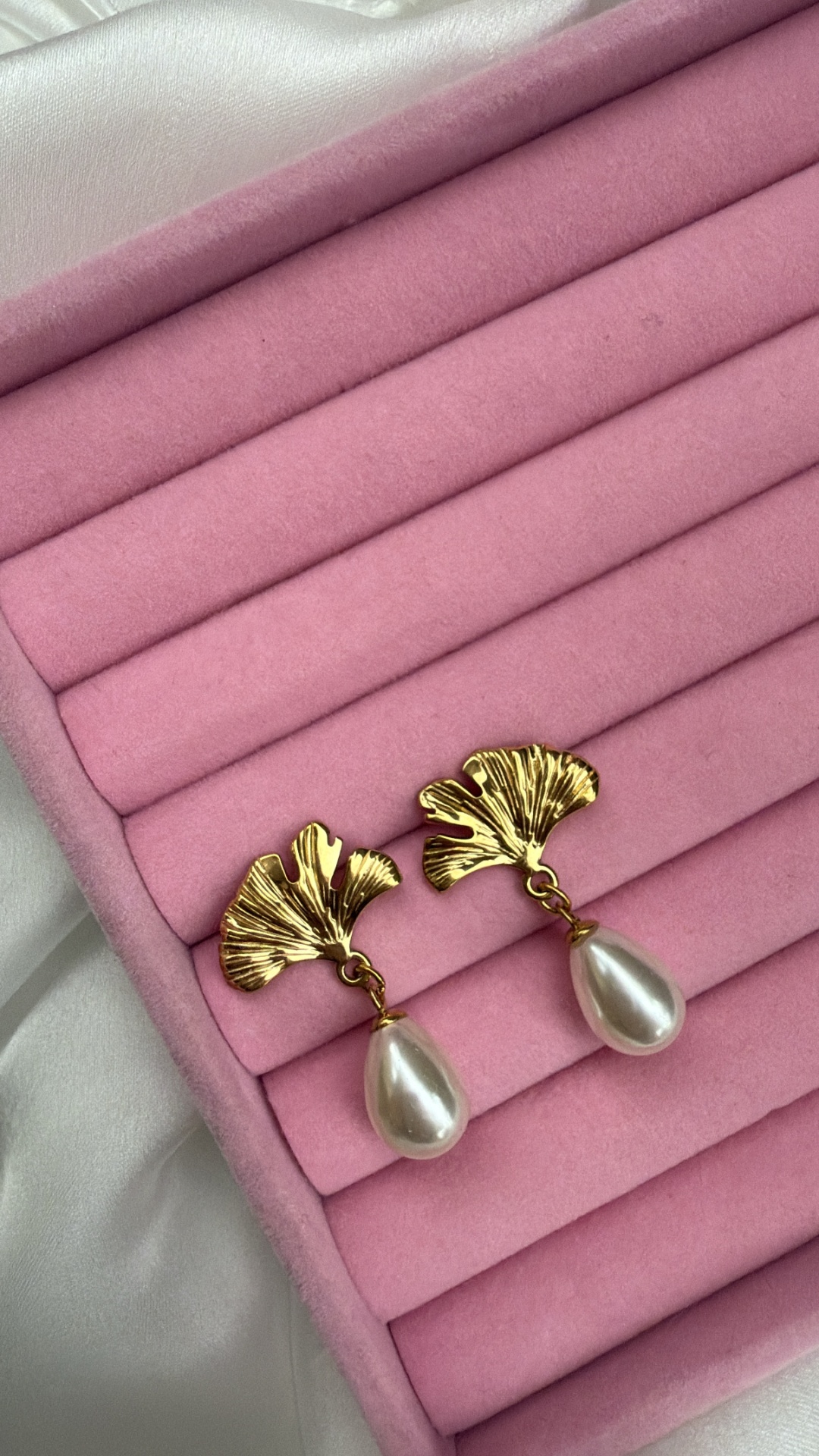 Brincos dourados com folha e pérola sobre estojo rosa