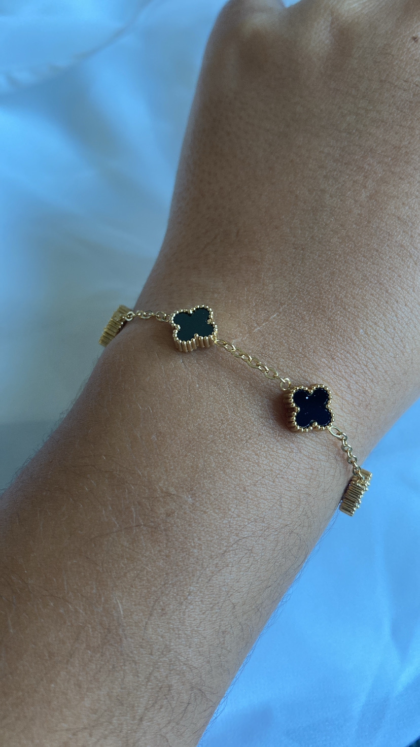 Pulseira dourada com trevos pretos no pulso