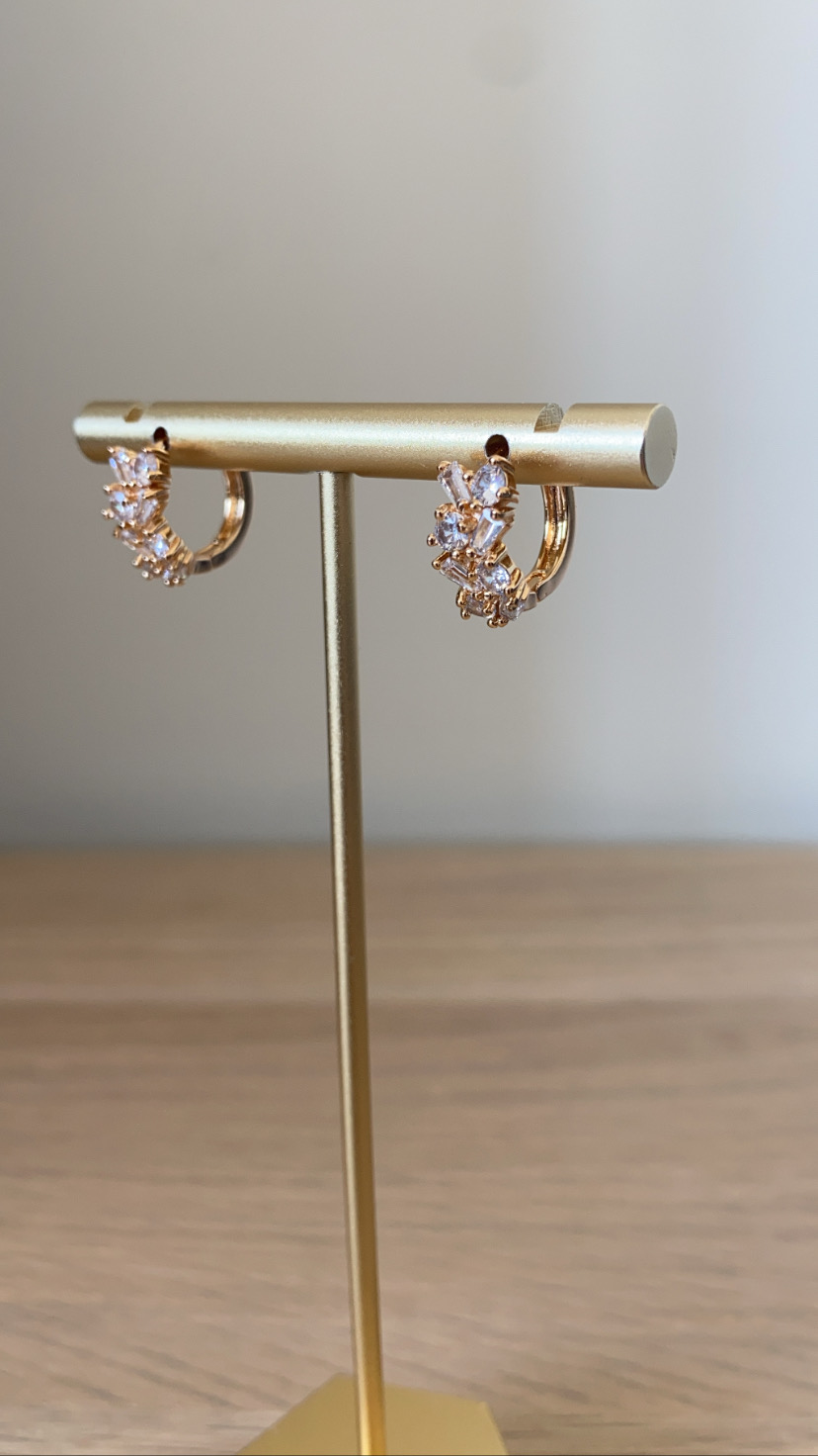 Brincos de argola dourados com pedras transparentes num suporte metálico dourado