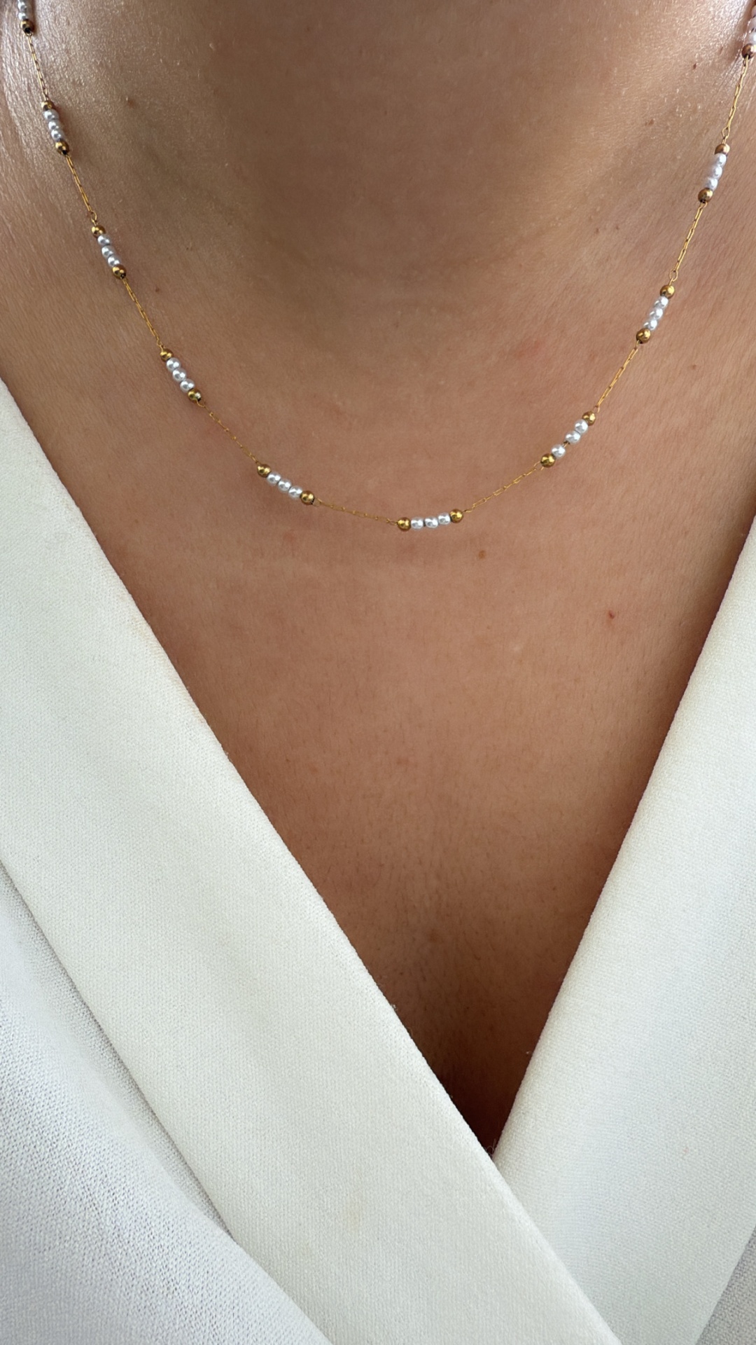 Colar dourado com pérolas pequenas ao pescoço