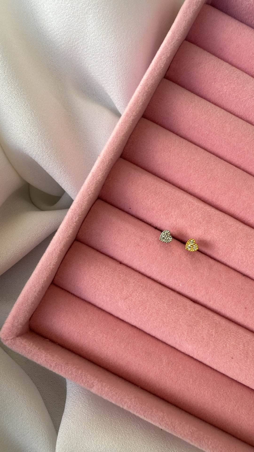 Brincos em forma de coração prateado e dourado numa caixa de veludo rosa.