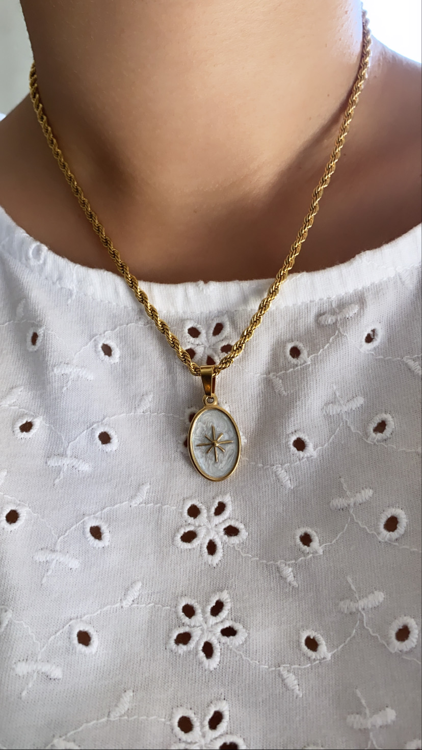 Colar dourado com pendente oval branco com estrela usado sobre blusa branca bordada
