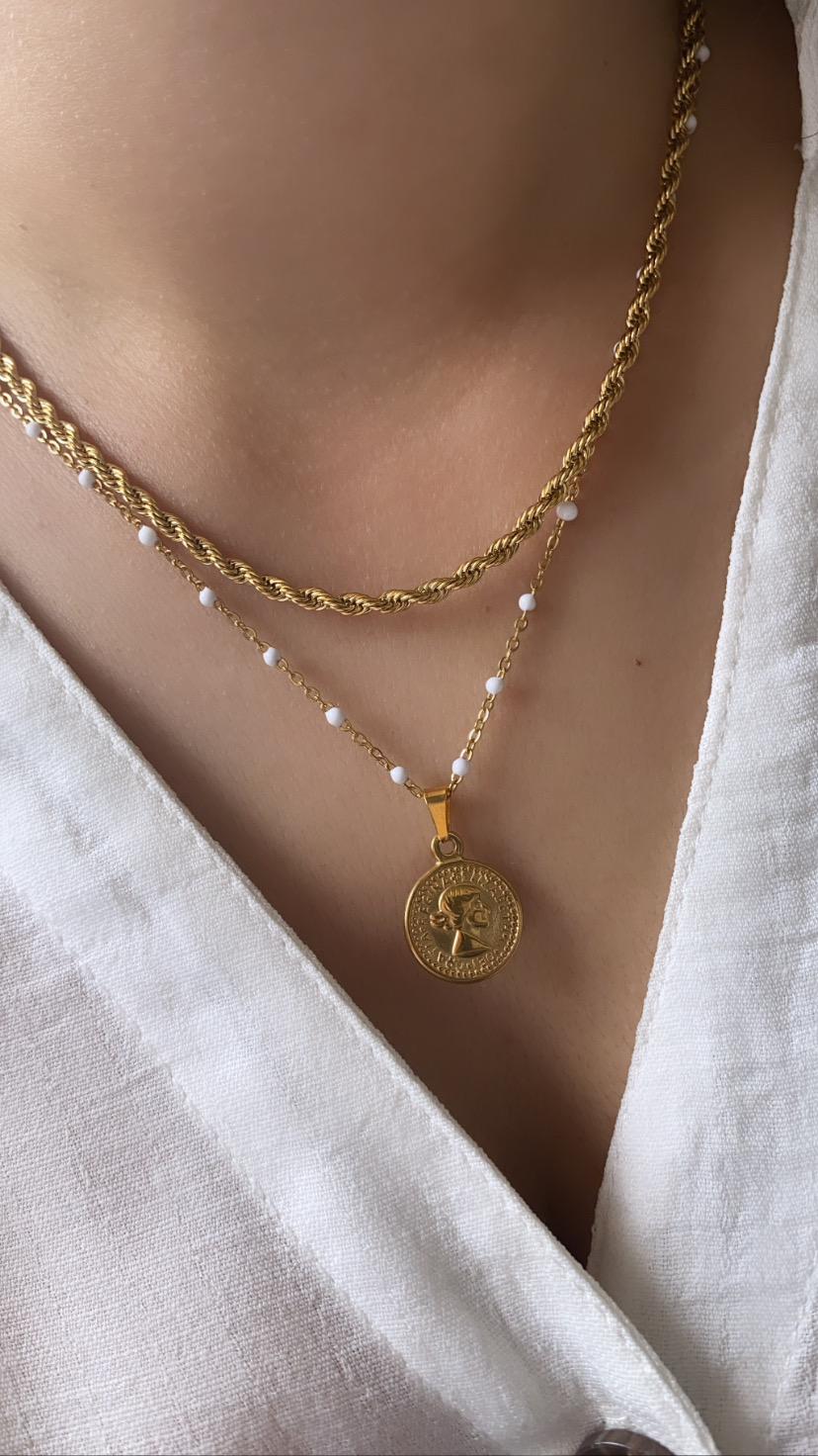 Colares dourados com pérolas e pendente circular em tecido branco.