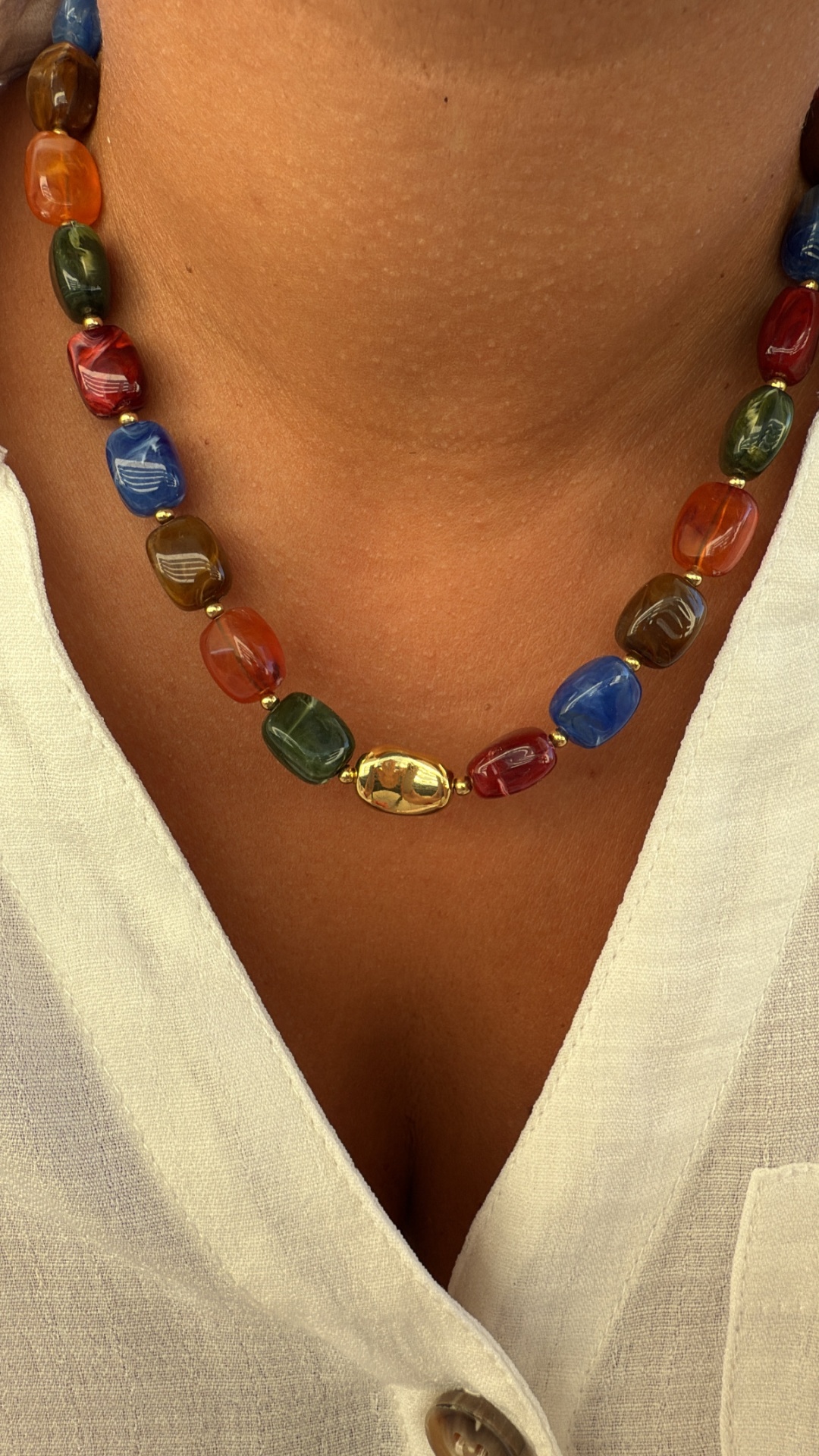 Colar colorido com conta dourada central sobre camisa branca