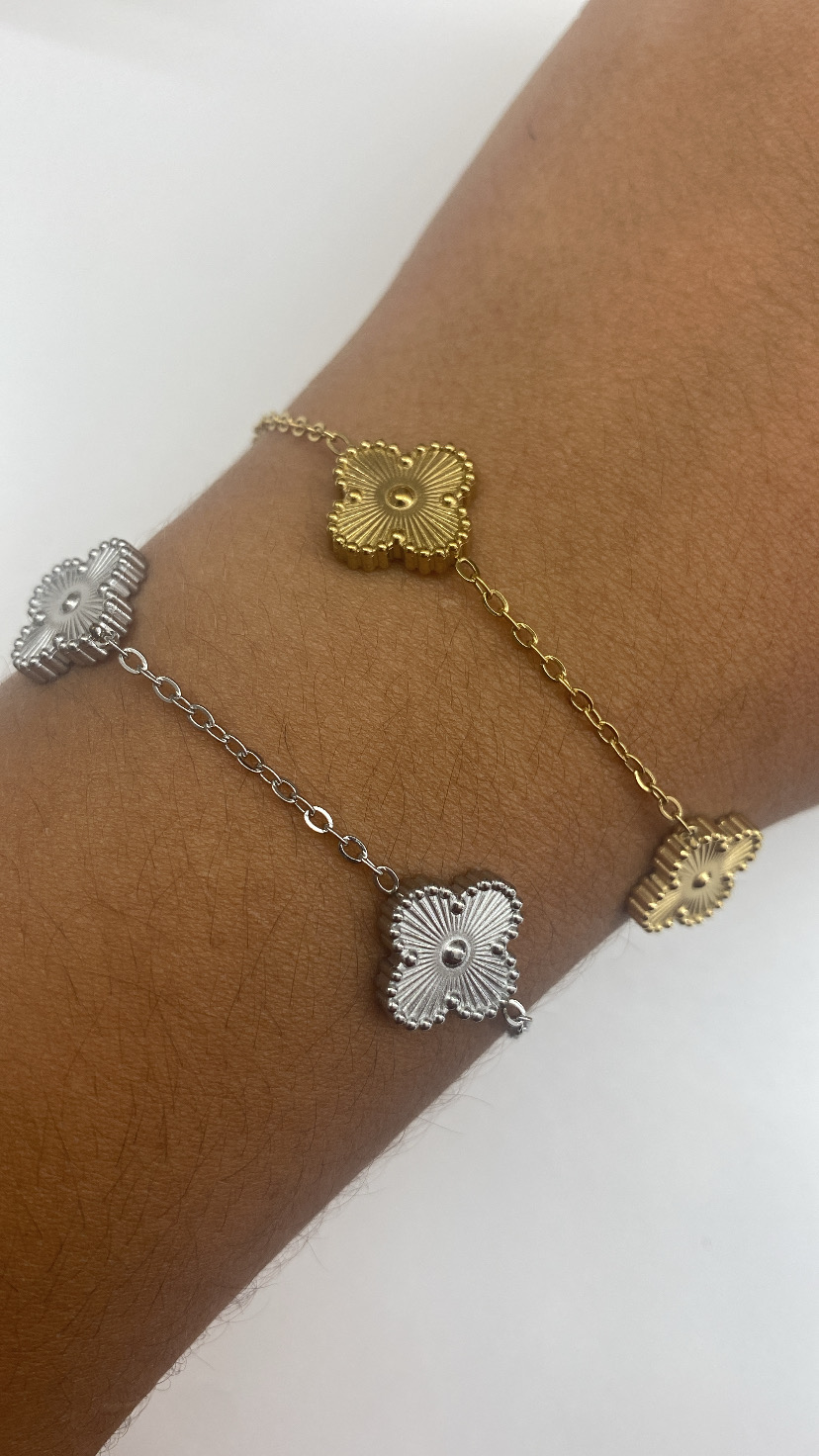 Pulseiras dourada e prateada com pendentes de flor no pulso.