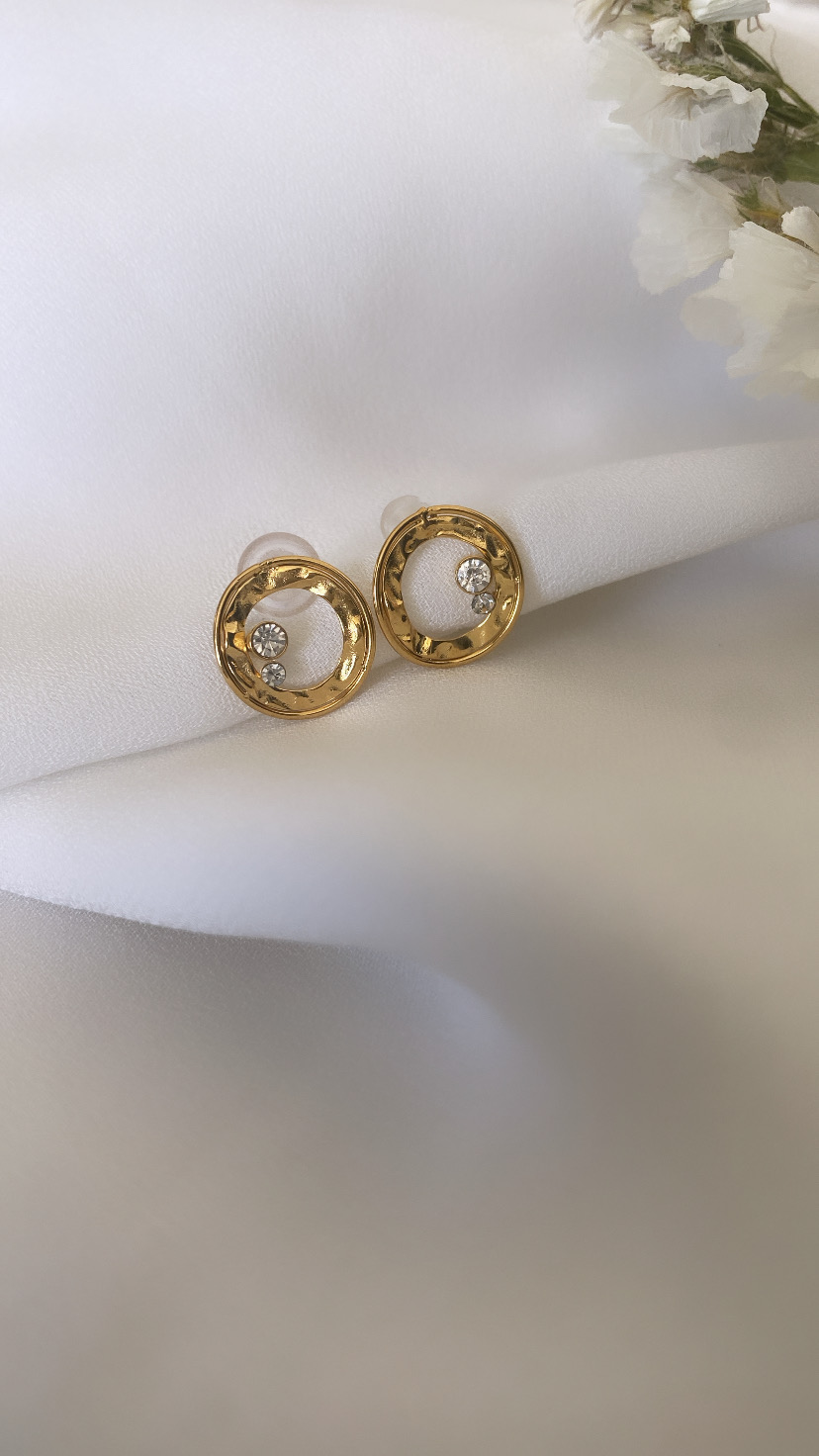 Brincos redondos dourados com pedras brilhantes sobre tecido branco