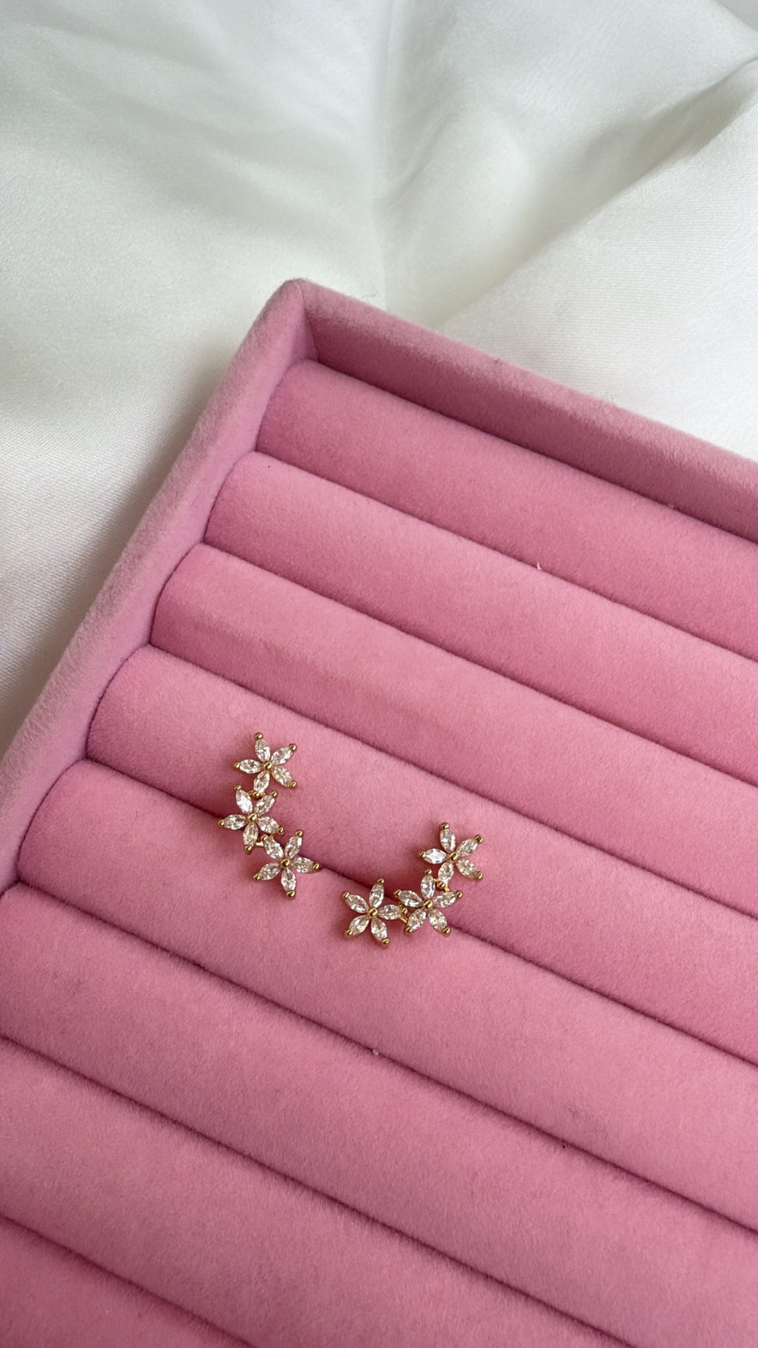 Brincos florais dourados com pedras em bandeja rosa.