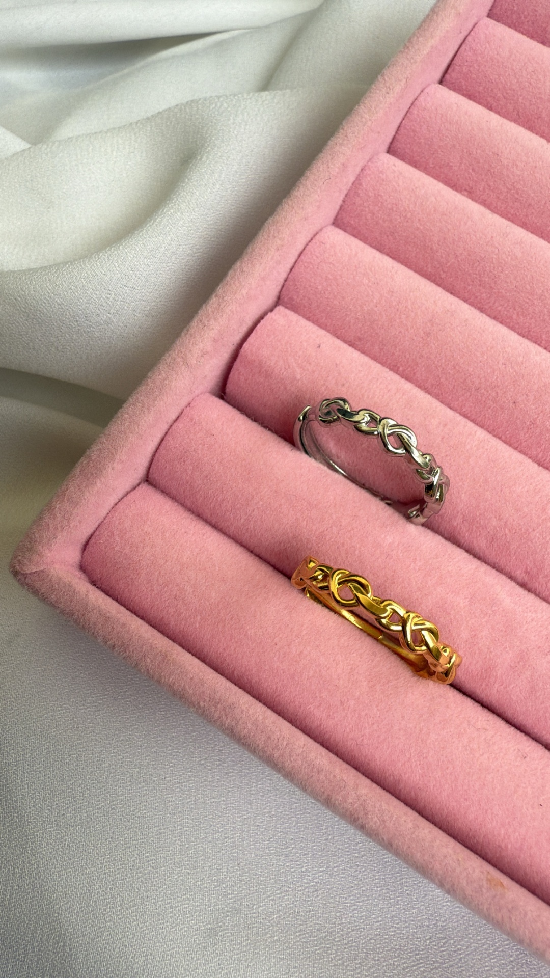 Duas alianças entrelaçadas, prateada e dourada, numa caixa rosa acolchoada.
