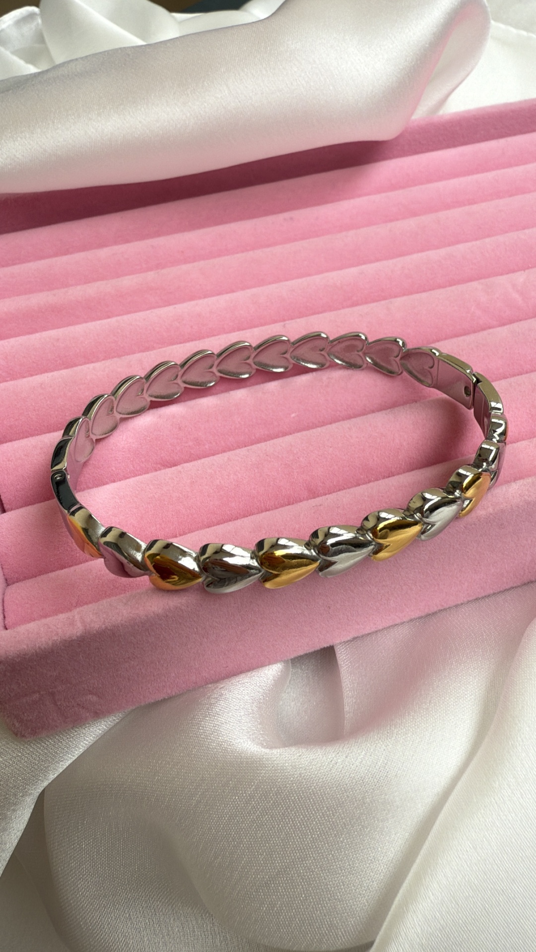 Pulseira com corações dourados e prateados sobre caixa de veludo rosa e tecido branco
