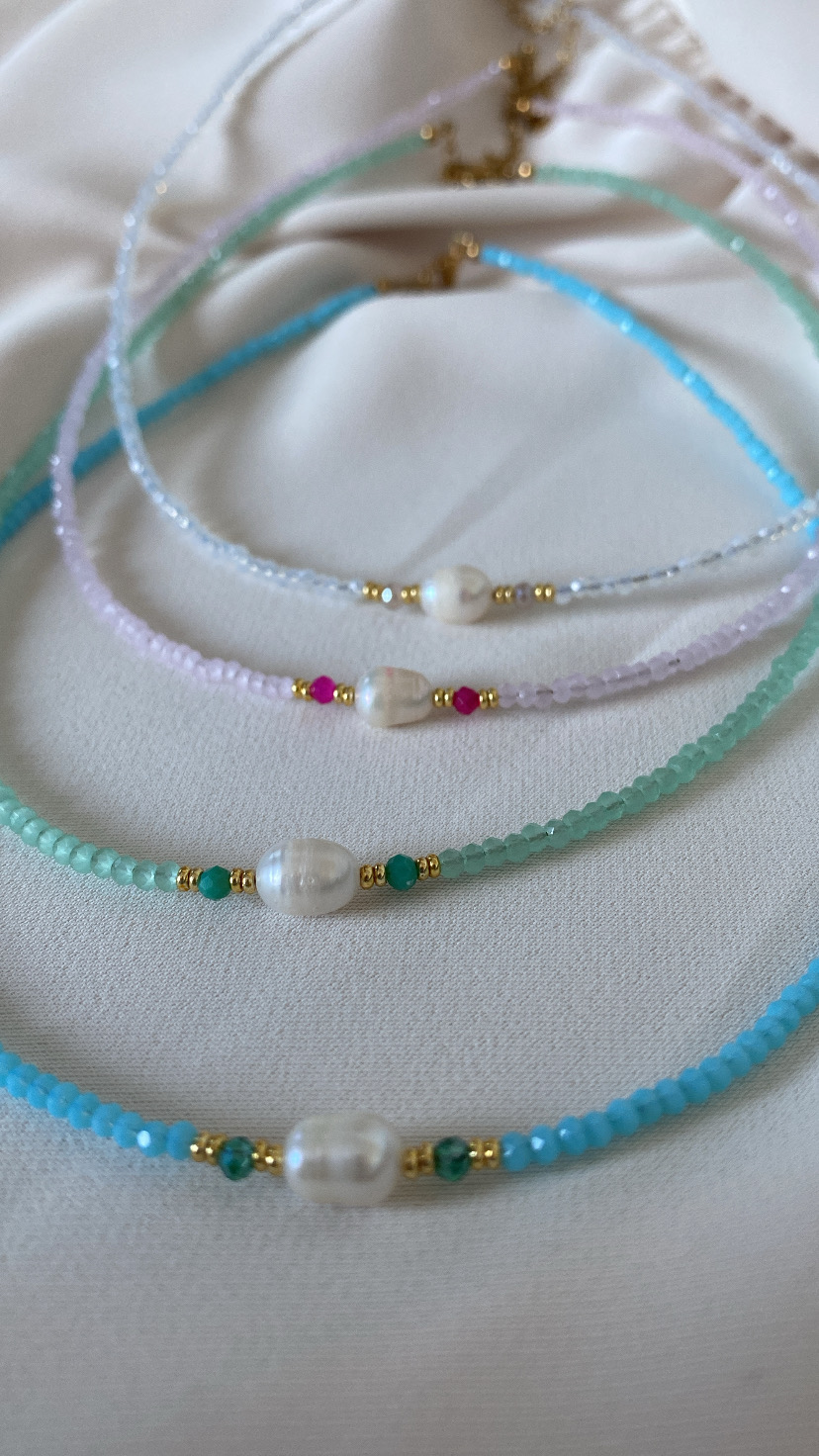 Colares com contas coloridas e pérolas centrais sobre tecido branco